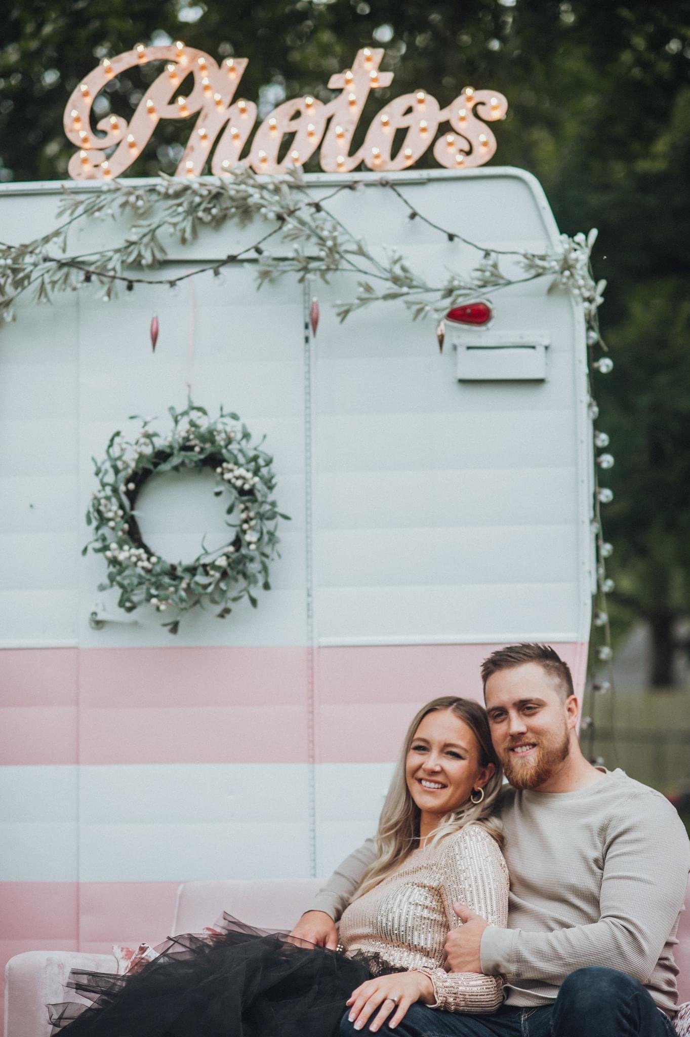 Liz and her husband sitting in front of a pink vintage camper decorated for Christmas
