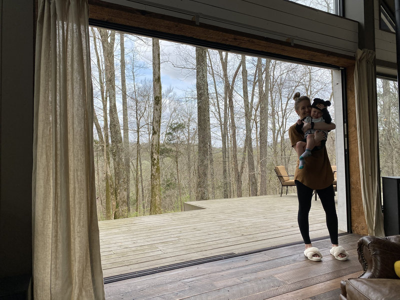 Liz on a cabin deck with her toddler beside a wall of glass